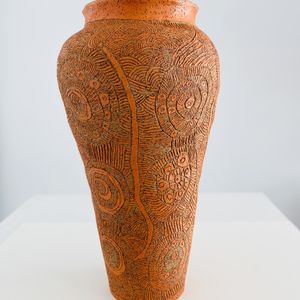 A large orange ceramic vessel, engraved with swirling patterns