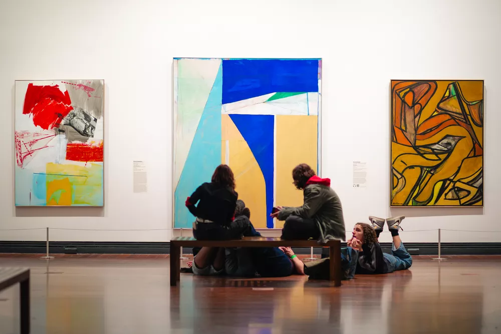 Group of teenagers casually sitting and laying down on the exhibition floor looking at artwork.