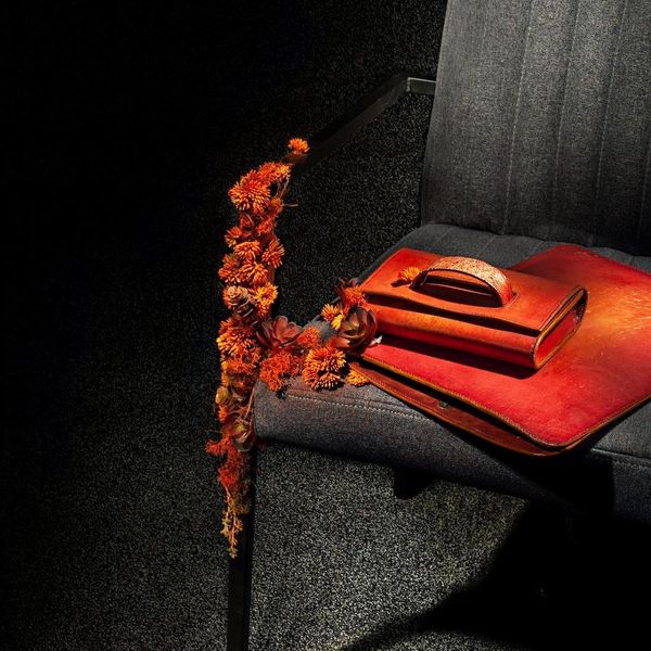 An orange leather handbag and satchel on a grey chair decorated with orange dried flowers