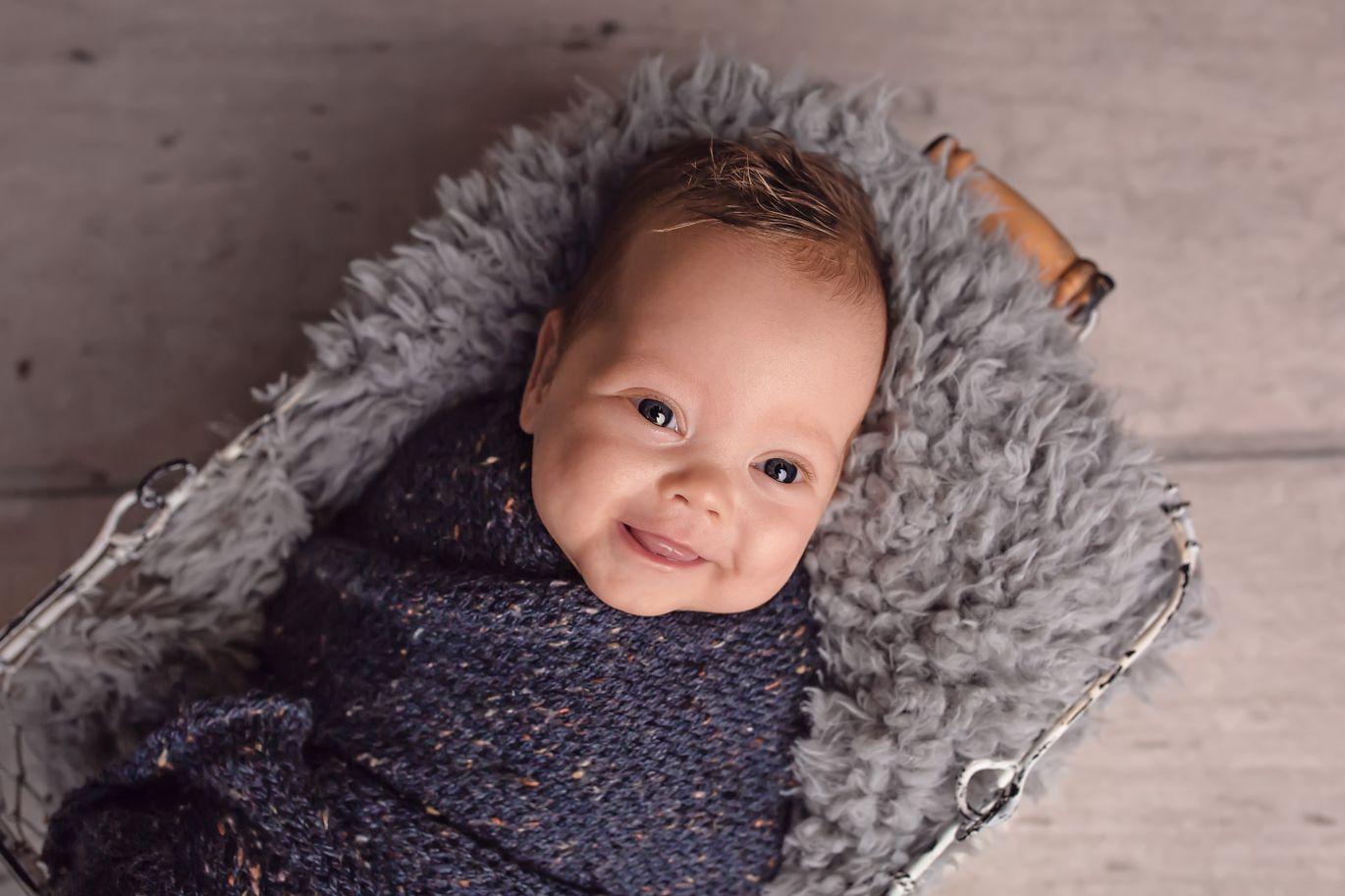 A baby lies on a rug and smiles up at the camera. 
