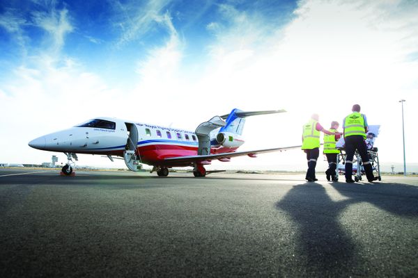A jet aircraft with an RFDS logo. People in high-vis clothing push a hospital stretcher with a person lying on top. 