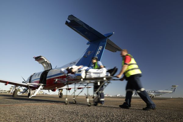 Two men in RFDS uniforms push a stretcher towards a RFDS plane. 