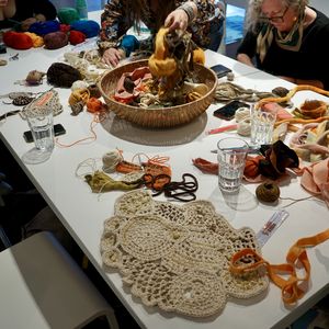 A table full of colourful textile materials and crochet with makers sat around it just out of shot