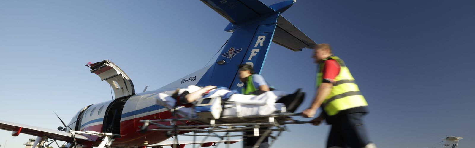 Two men in RFDS uniforms push a stretcher towards a RFDS plane. 