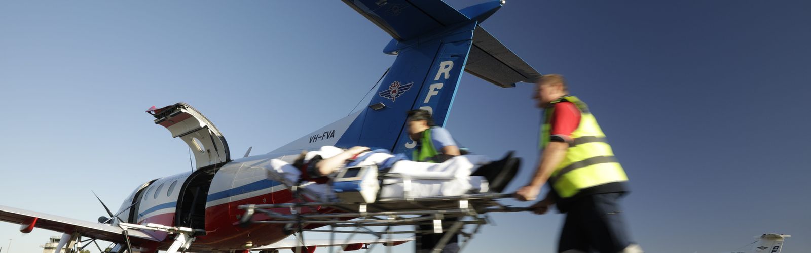 Two men in RFDS uniforms push a stretcher towards a RFDS plane.