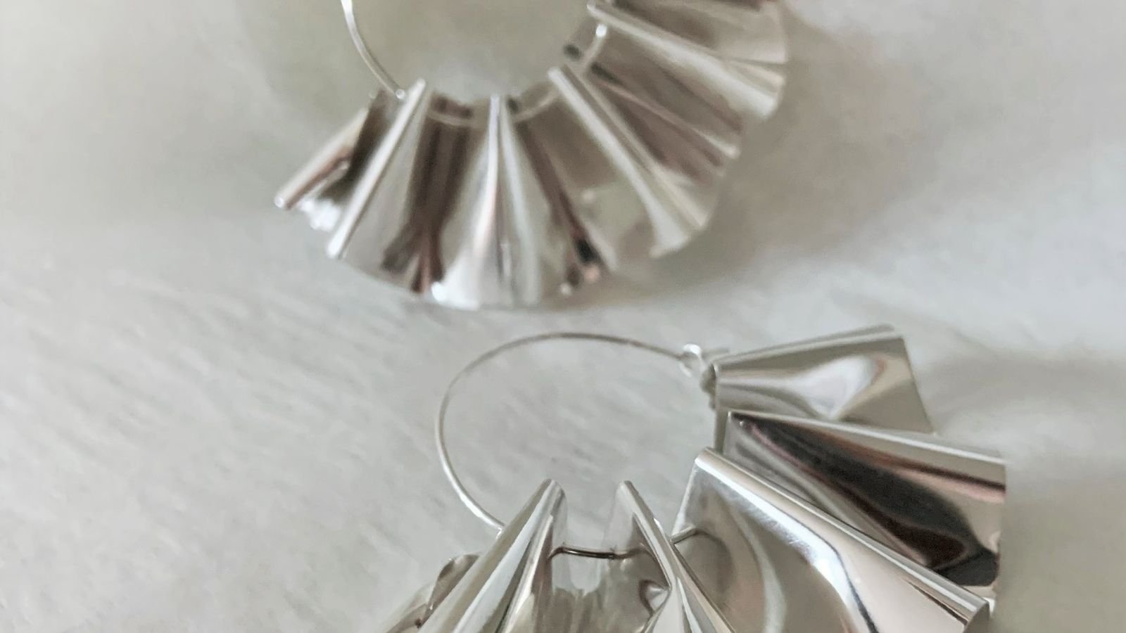 A pair of shiny rippled sheet silver earrings on silver hoops, on a white background.
