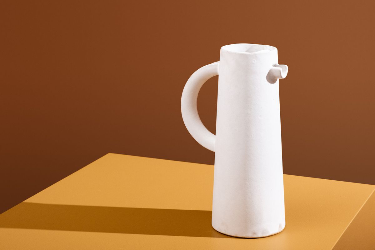 Photo of a tall white ceramic jug on a brown background