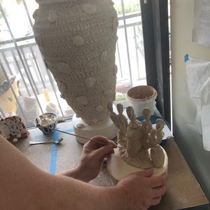 Hands adding detail to a clay object with a skewer