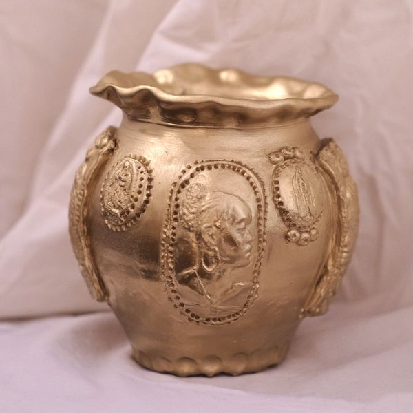 A gold vase or urn, imprinted with the portrait image of an important Black women with her hair in a bun and large hoop earrings