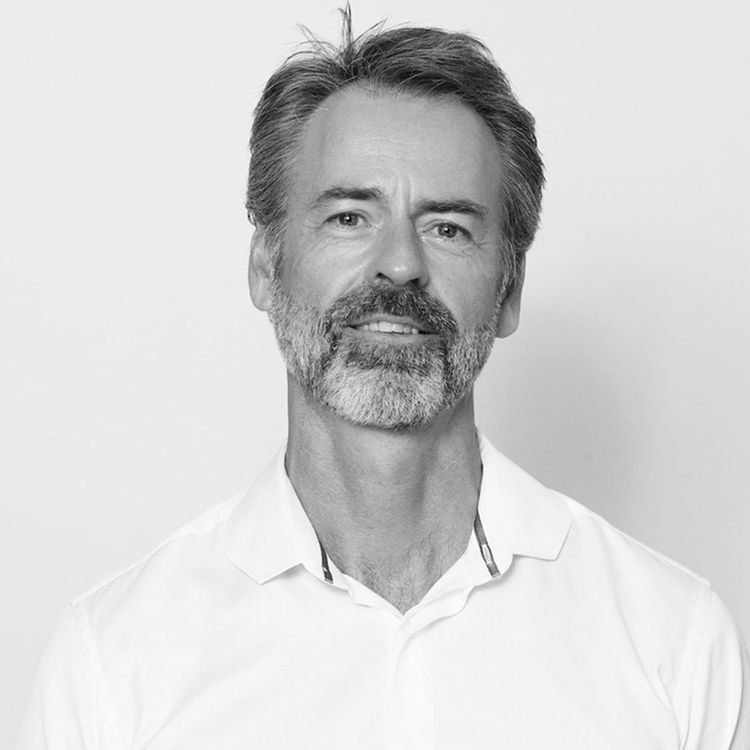 Photo of a middle aged man wearing a white shirt with grey hair and beard against a white background.