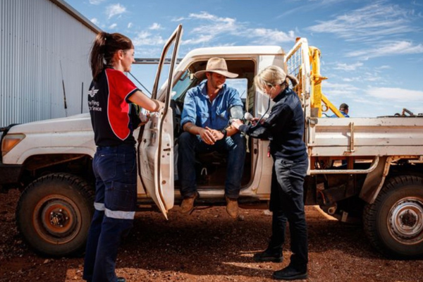 a nurse in an RFDS shirt and a doctor checking the heart rate of a patient who is sitting in a ute