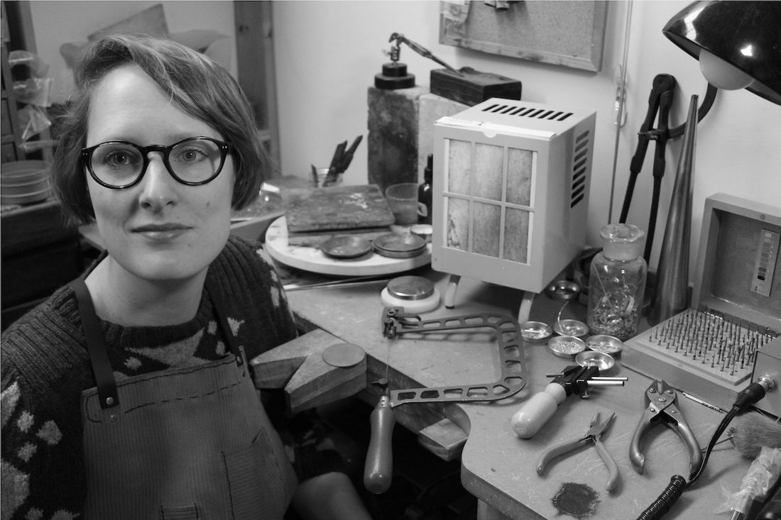 A black and white portrait of Claire McArdle sitting at her work bench covered in tools
