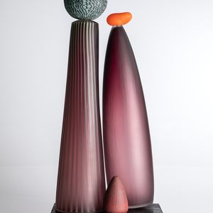 Three glass sculptures displayed on a black base, showcasing intricate designs and vibrant colours in purple and red hues. Emphasising their unique shapes and translucent qualities