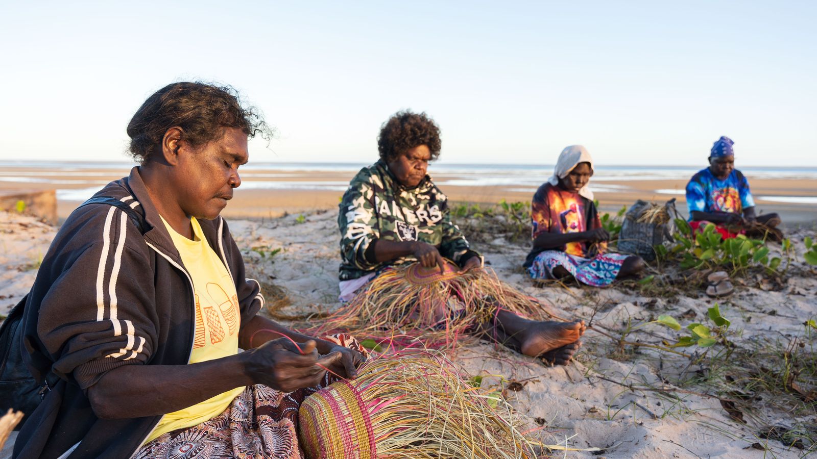 Four first nations women weaving baskets on the beach
