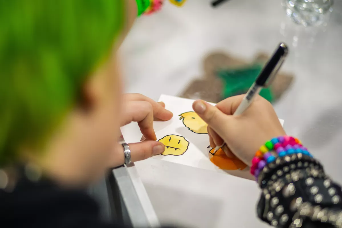 Young person drawing smiley faces on paper.