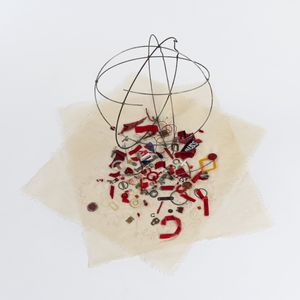 circular metal frame sitting on cream textile square cut off's with an assortment of red small found objects