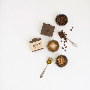Hand-made soap surrounded by mixing spoon, dishes, coffee beans, honey, cinnamon sticks.