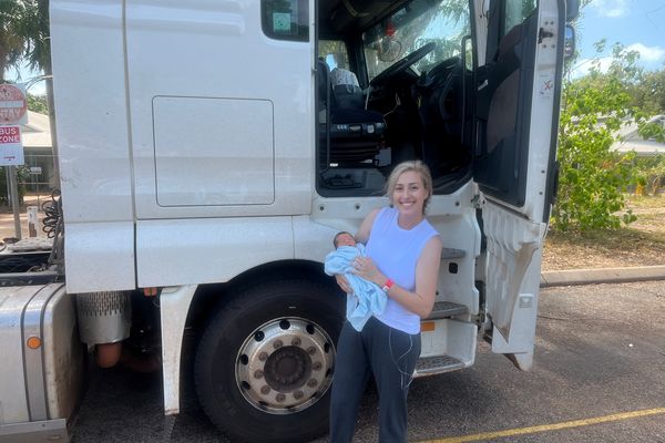 Ella holding baby Lucas in front of prime mover truck.