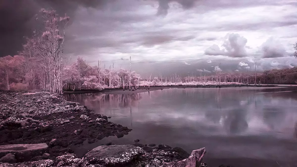 A landscape photograph in vivid pinks and purples of a lake with a stormy sky