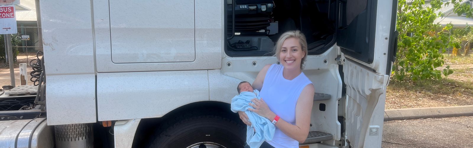 Ella holding baby Lucas in front of prime mover truck.