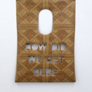 A wooden like surface featuring the phrase "How did we get here?" engraved on its surface