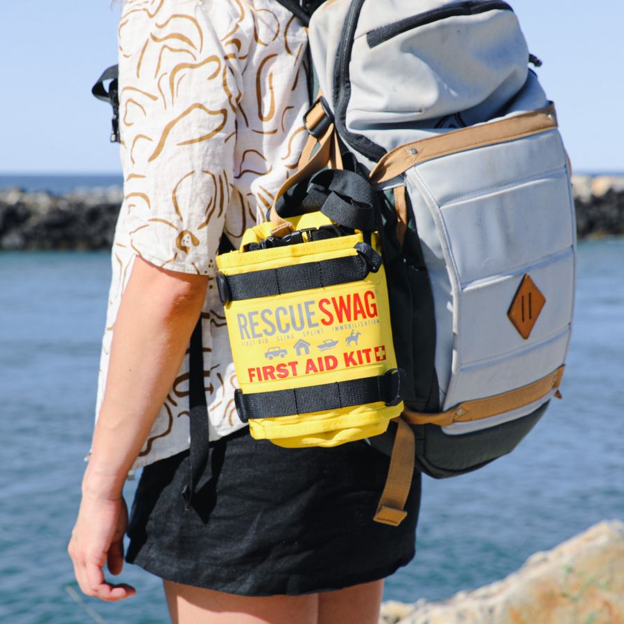 Dr Shaun Francis is standing in front of a green shrub wearing his uniform and holding a yellow Rescue Swag first aid kit