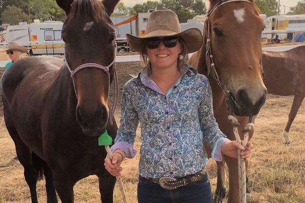 A young woman smiles. She is standing next to two horses. 