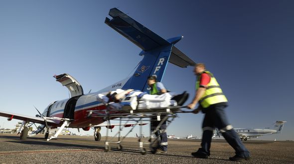 Two men in RFDS uniforms push a stretcher towards a RFDS plane. 