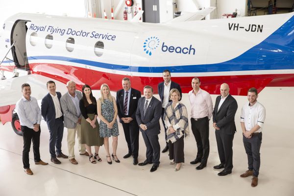 Two men in suits stand in front of an aircraft with a BEACH Energy logo on the side. The men are smiling. 