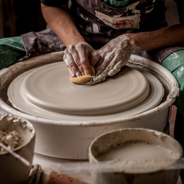 Photo of hand pushing down onto clay on a potters wheel with a green background