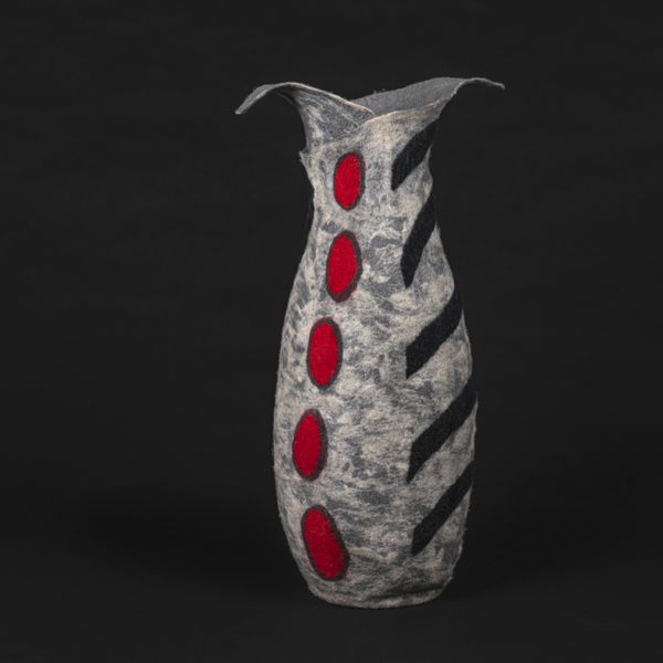 A grey coloured felted vessel in the form of a tall free standing vase with red dots and black stripes.