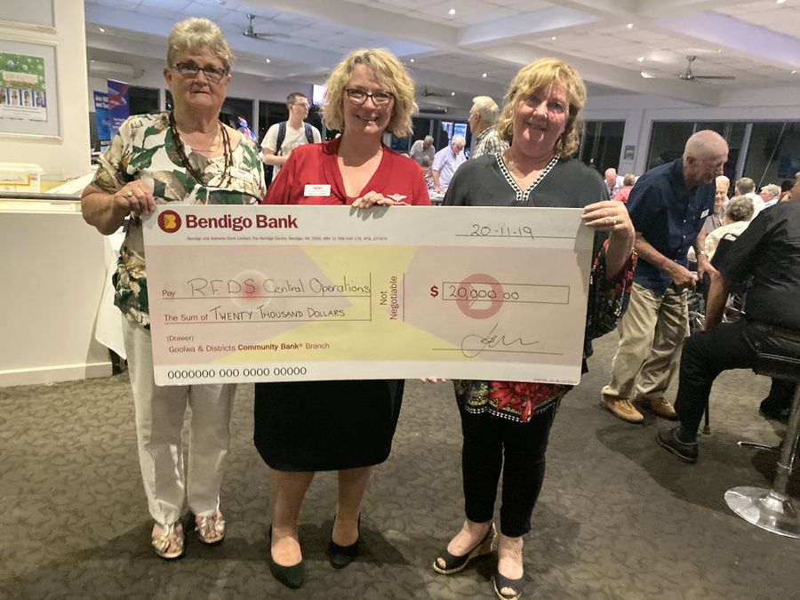 3 females hold an oversized cheque for $20,000 and smile. 