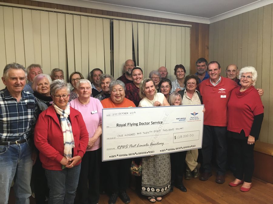 A group of people holding an oversized cheque smile at the camera. The cheque is made out to the RFDS for $128,000. 
